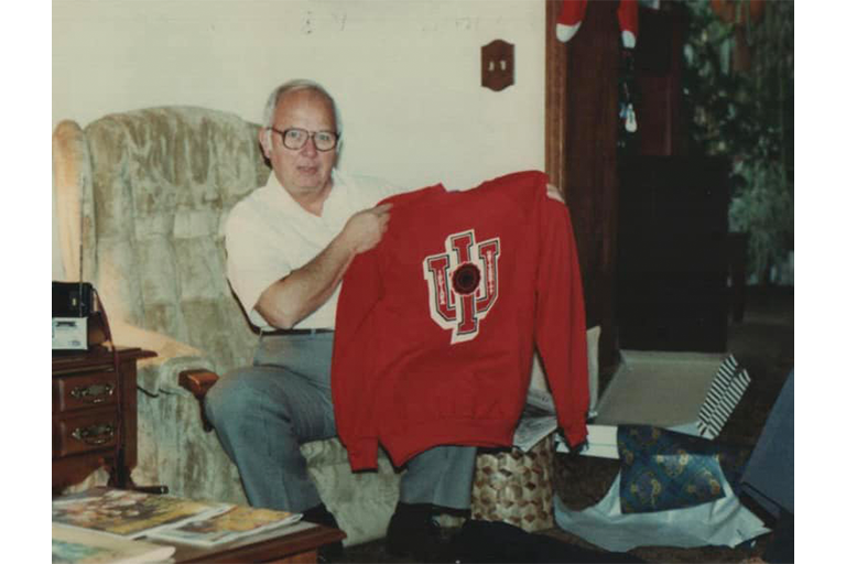 A man with white hair and glasses happily shows a red IU sweatshirt he just received for Christmas in this vintage photograph.