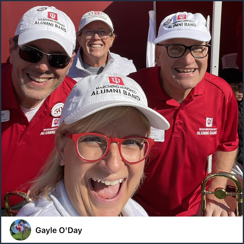 A selfie of four people all wearing white hats that feature the IU logo and “Marching Hundred Alumni Band.” All are smiling and dressed in various IU spirit wear.